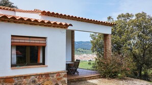 Un edificio con base de piedra, techo de tejas, ventana con persianas y un patio con mesa y sillas.