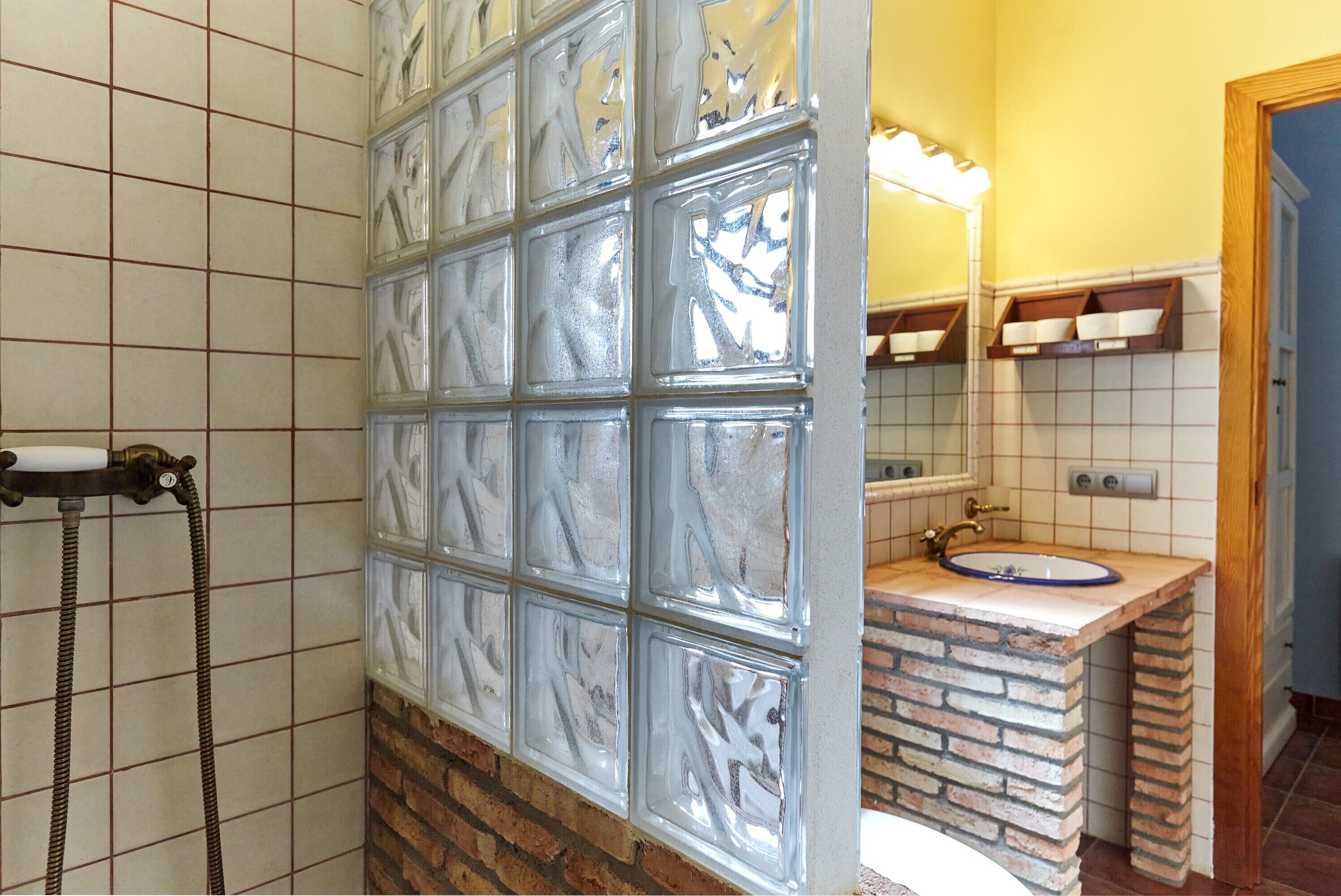 Un baño con separador de vidrio, ducha con manguera, lavamanos de color azul y espejo sobre el lavamanos.