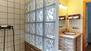 Un baño con separador de vidrio, ducha con manguera, lavamanos de color azul y espejo sobre el lavamanos.