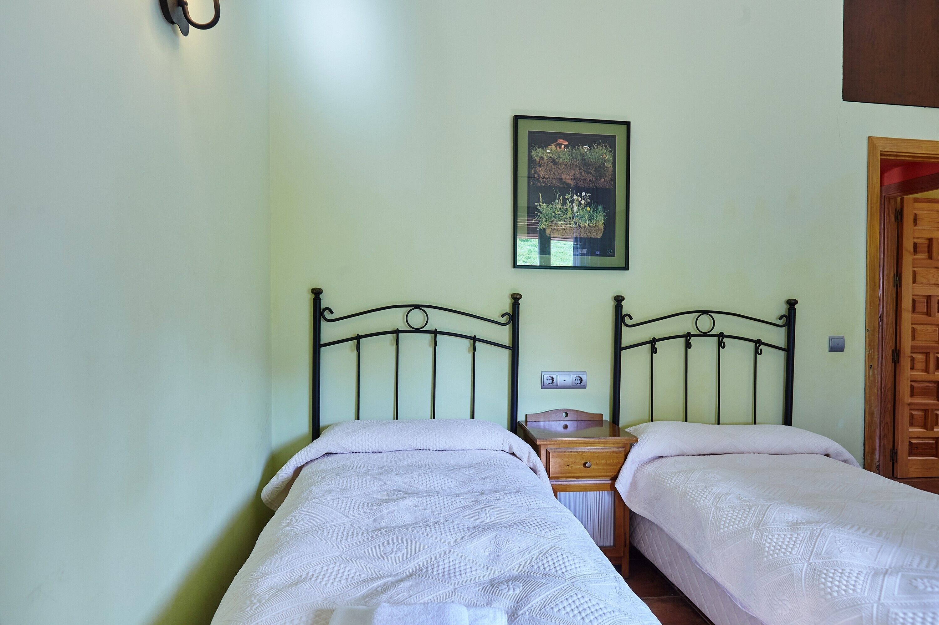 Una habitación con dos camas, una mesita de noche pequeña, un cuadro colgado en la pared y una puerta de madera.
