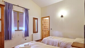 A bedroom with two beds, a radiator, a wooden door, and a window with curtains.