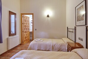 A bedroom with two beds, a radiator, a wooden door, and a wall-mounted light fixture.