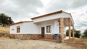A single-story house with a stone foundation, a tiled roof, and a covered porch with chairs.