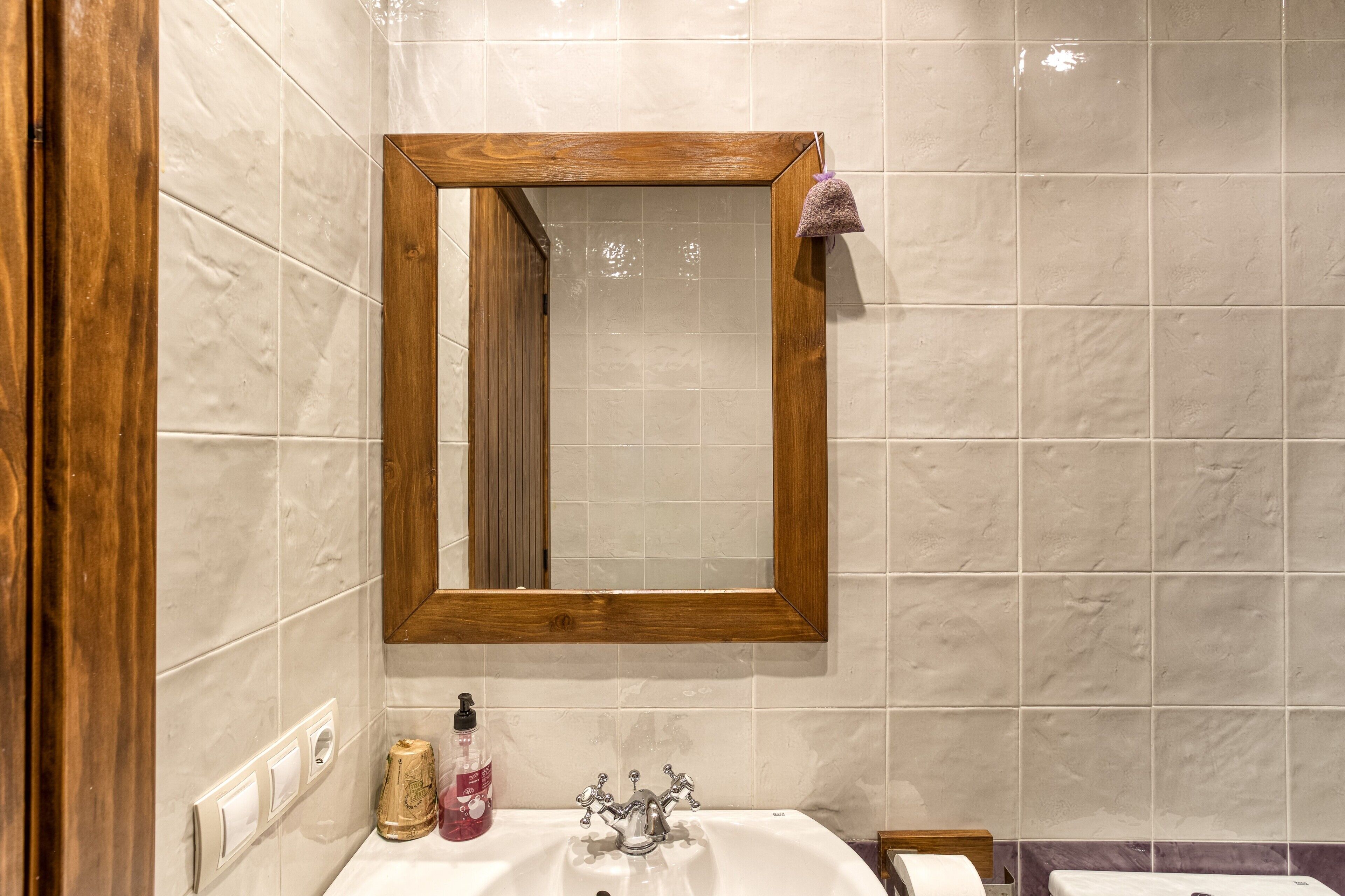 Une salle de bain avec un miroir encadré en bois, un lavabo blanc et un mur recouvert de carreaux de marbre.