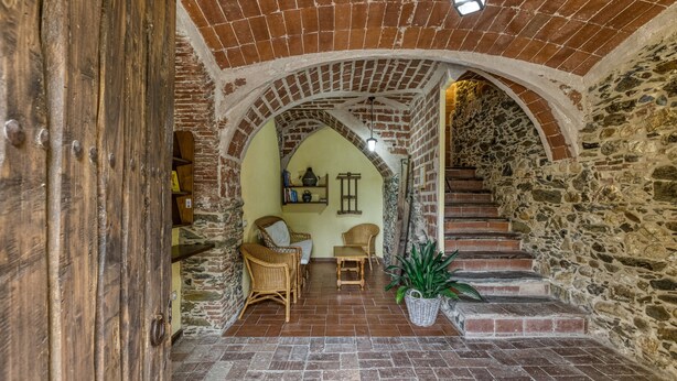 Un interior con una escalera de piedra, una puerta de madera y una zona de estar con mobiliario de mimbre.