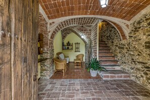 Un interior con una escalera de piedra, una puerta de madera y una zona de estar con mobiliario de mimbre.