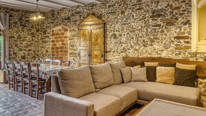 Una habitación con paredes de piedra, una mesa de madera para comer, sillas y un sofá.