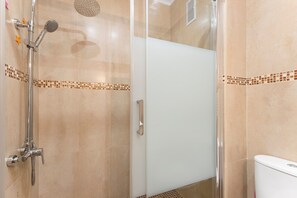 Ducha con cabezal de ducha de mano, cabezal de ducha empotrado y mampara de vidrio.