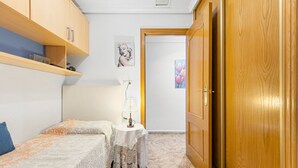 Un dormitorio con cama, una mesita de noche con lámpara, un armario y una puerta que da a otra habitación.