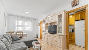 Sala de estar con sofá, televisión y área de cocina con armarios y refrigerador.