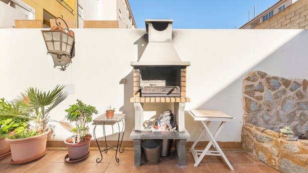 Un patio exterior con un horno de ladrillo, plantas en macetas, una mesita y un muro de piedra.