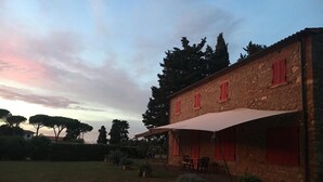 Ein rustikales Steinhaus mit roten Fensterläden, einer Terrasse mit Gartenmöbeln und einem großen Sonnenschirm.