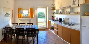 Eine Küche mit Esstisch, Stühlen, einem Kühlschrank, einer Spüle und einem Fenster mit Vorhängen.