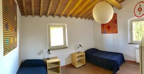 Una habitación con dos camas, una ventana, un escritorio con lámpara y una lámpara colgante.