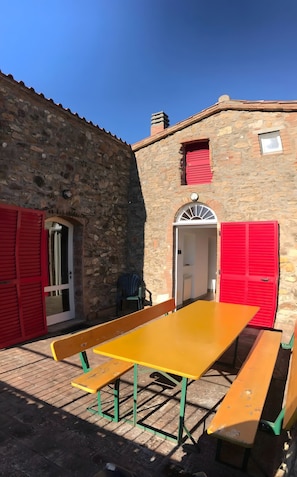 A stone building with red shutters, a bench, and a table.