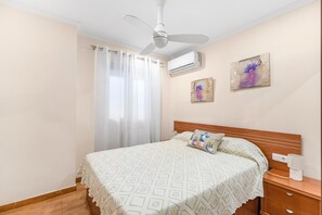 A bedroom with a bed, a nightstand, a wall-mounted air conditioner, and a ceiling fan.