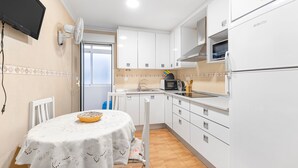 A compact kitchen with white cabinets, a microwave, a refrigerator, and a dining area with a table and chairs.