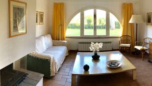 A room with a sofa, a table with a vase and bowl, a chair, and a window with curtains. - Apartment 'Arco' with Shared Garden and Wi-Fi (Bibbona)