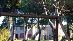 A swing set with two swings, a stone building with red shutters, and a grassy area. - Apartment 'Arco' with Shared Garden and Wi-Fi (Bibbona)