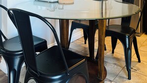 Une cuisine compacte avec une table à manger au plateau en verre, des chaises noires, un réfrigérateur en acier inoxydable et un ventilateur de plafond.