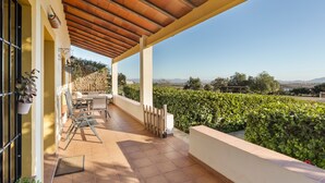 A covered outdoor patio with a view of a vineyard, a table and chairs, and a pergola structure.