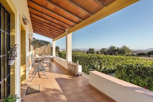 Une terrasse extérieure couverte avec vue sur un vignoble, une table et des chaises, ainsi qu’une structure en forme de pergola.