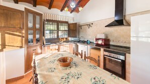A kitchen with wooden cabinets, a dining table with a floral tablecloth, a stove, and a built-in oven.