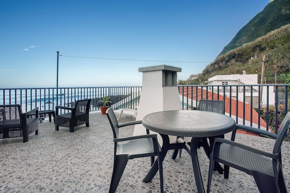 A terrace with a table and chairs, a potted plant, and a view of the sea.