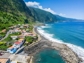 A coastal village with houses along the beach, a rocky shoreline, and a mountainous backdrop.