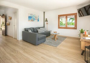Un salon moderne avec un canapé d’angle gris, une petite table ronde, un lampadaire et une fenêtre donnant sur un paysage verdoyant.