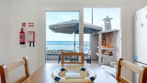 A dining table with a life preserver, chairs, a fire extinguisher, and a view of the ocean through a glass door. - Apartment 'Beach Front Flat' with Sea View, Private Terrace and Wi-Fi (São Vicente)