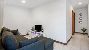A living room with a sofa, a TV on a white stand, and a small table with decorative items. - Apartment 'Beach Front Flat' with Sea View, Private Terrace and Wi-Fi (São Vicente)