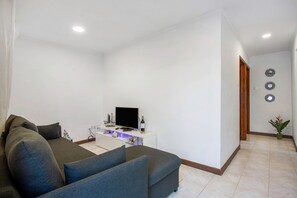 A living room with a sofa, a TV on a white stand, and a small table with decorative items.