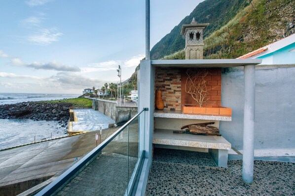 A coastal building with a balcony overlooking the sea, a stone structure, and a paved walkway.