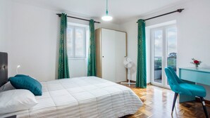 A bedroom with a bed, a desk, a chair, and a balcony with curtains. - Apartment 'Beach Front Flat' with Sea View, Private Terrace and Wi-Fi (São Vicente)