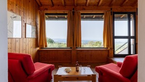 A wooden cabin room with two red sofas, a wooden table with a bottle and glasses, and large windows with curtains. - Villa 'Eleonora' with Private Pool, Private Garden and Wi-Fi (San Vivaldo)