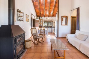 A living room with a fireplace, wooden furniture, a tiled floor, and a kitchen in the background.