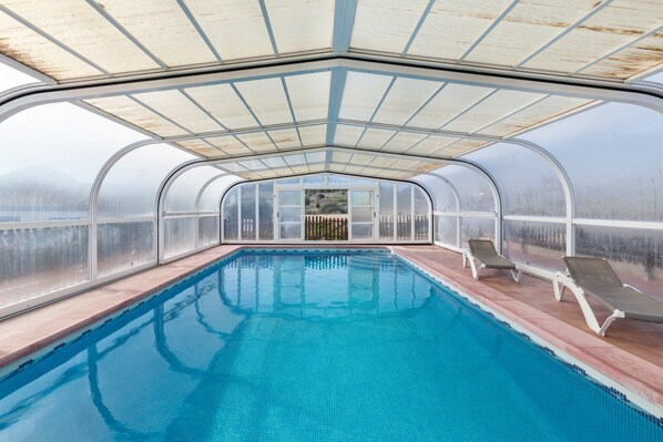 A transparent greenhouse structure with a pool and lounge chairs.