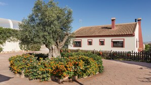 Una casa con techo de tejas, cerca blanca y un árbol en el jardín delantero.