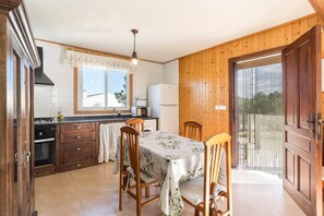 Une cuisine avec des meubles en bois, une table à manger avec des chaises, un réfrigérateur et une fenêtre donnant sur un beau paysage.