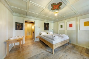 Un dormitorio con cama y mesita de noche de madera, una puerta que da a otra habitación y un techo con un detalle decorativo.