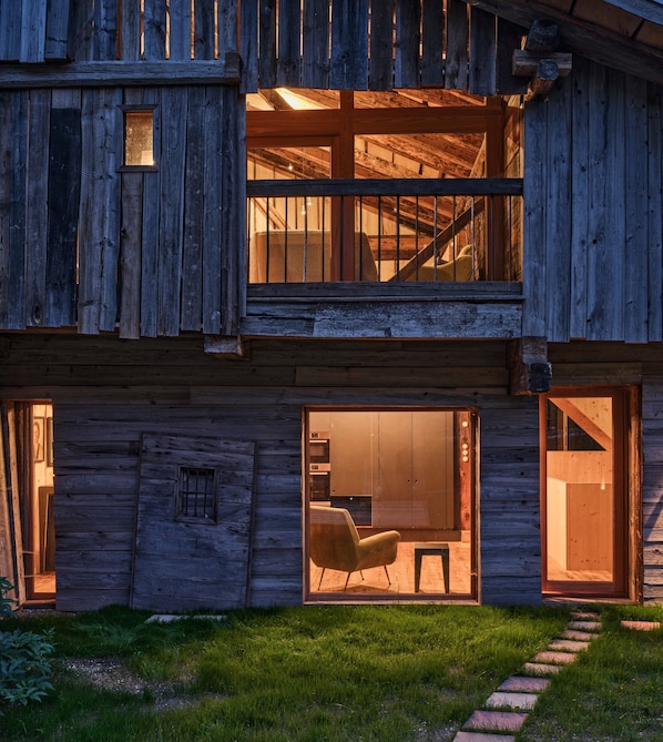 Un edificio rústico de madera con escaleras, ventanas amplias y un patio cubierto de césped.