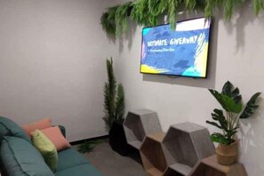 A living room with a flat-screen TV mounted on the wall, a green sofa, and a potted plant.