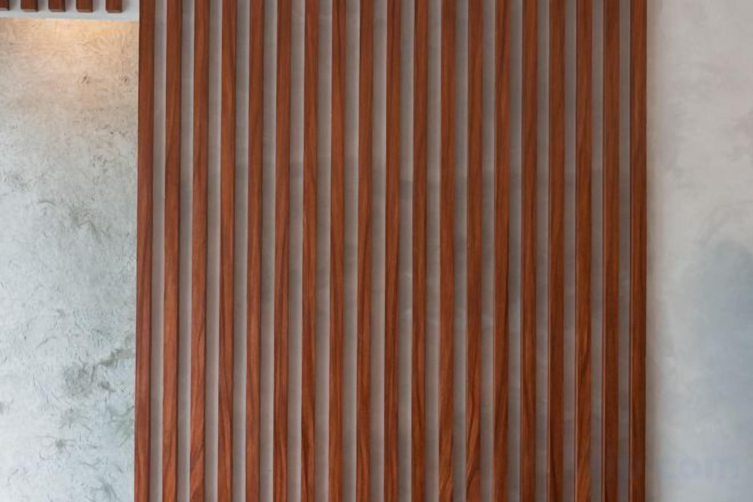 A vertical wooden slat wall with a textured concrete surface to the left.