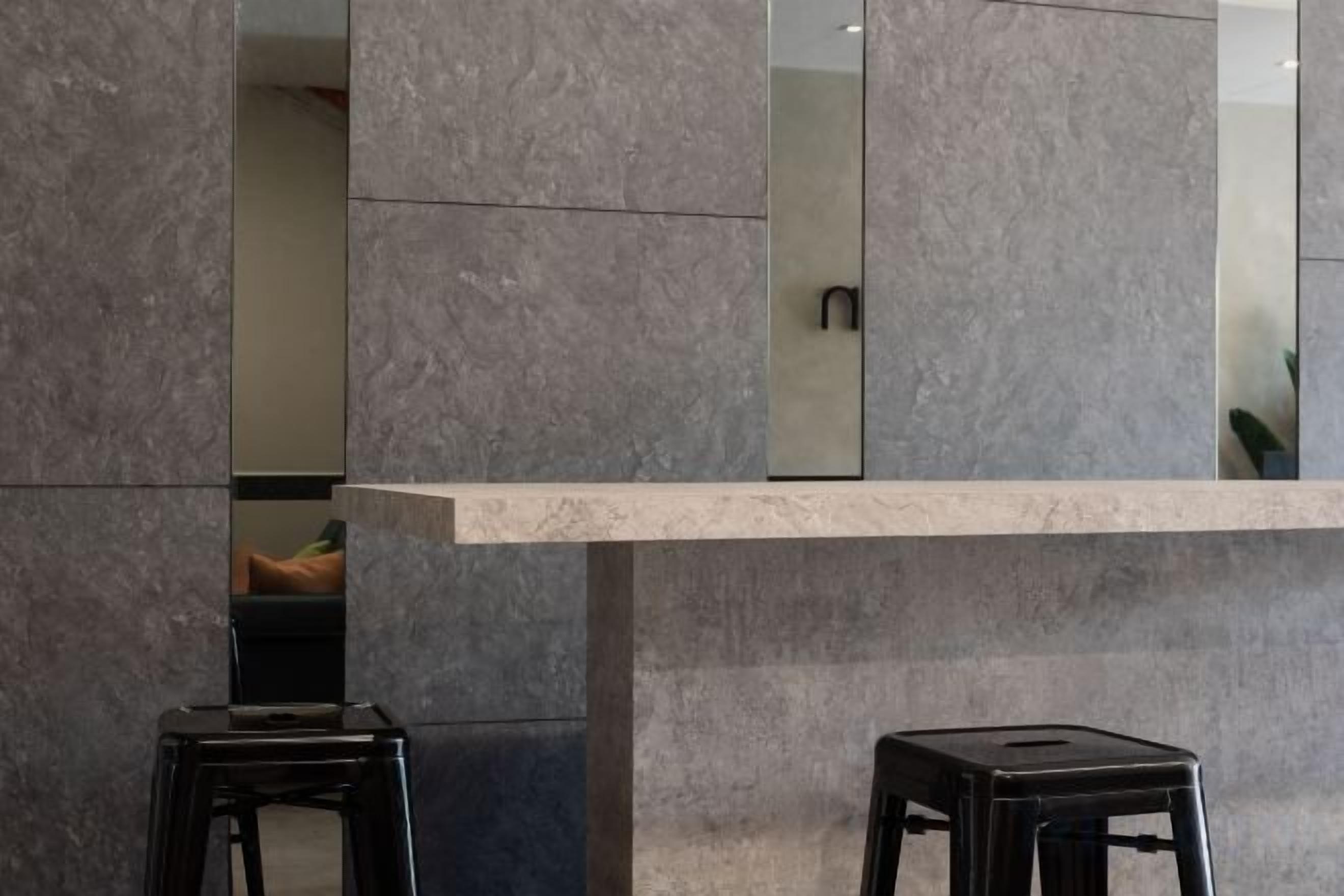 A modern interior with a marble column, a reflective surface, and two black stools.