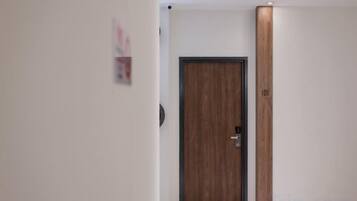 A hallway with a wooden door, a wall-mounted light fixture, and a door number.