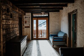 A rustic room with a wooden bench, a patterned sofa, and a view through a wooden door.