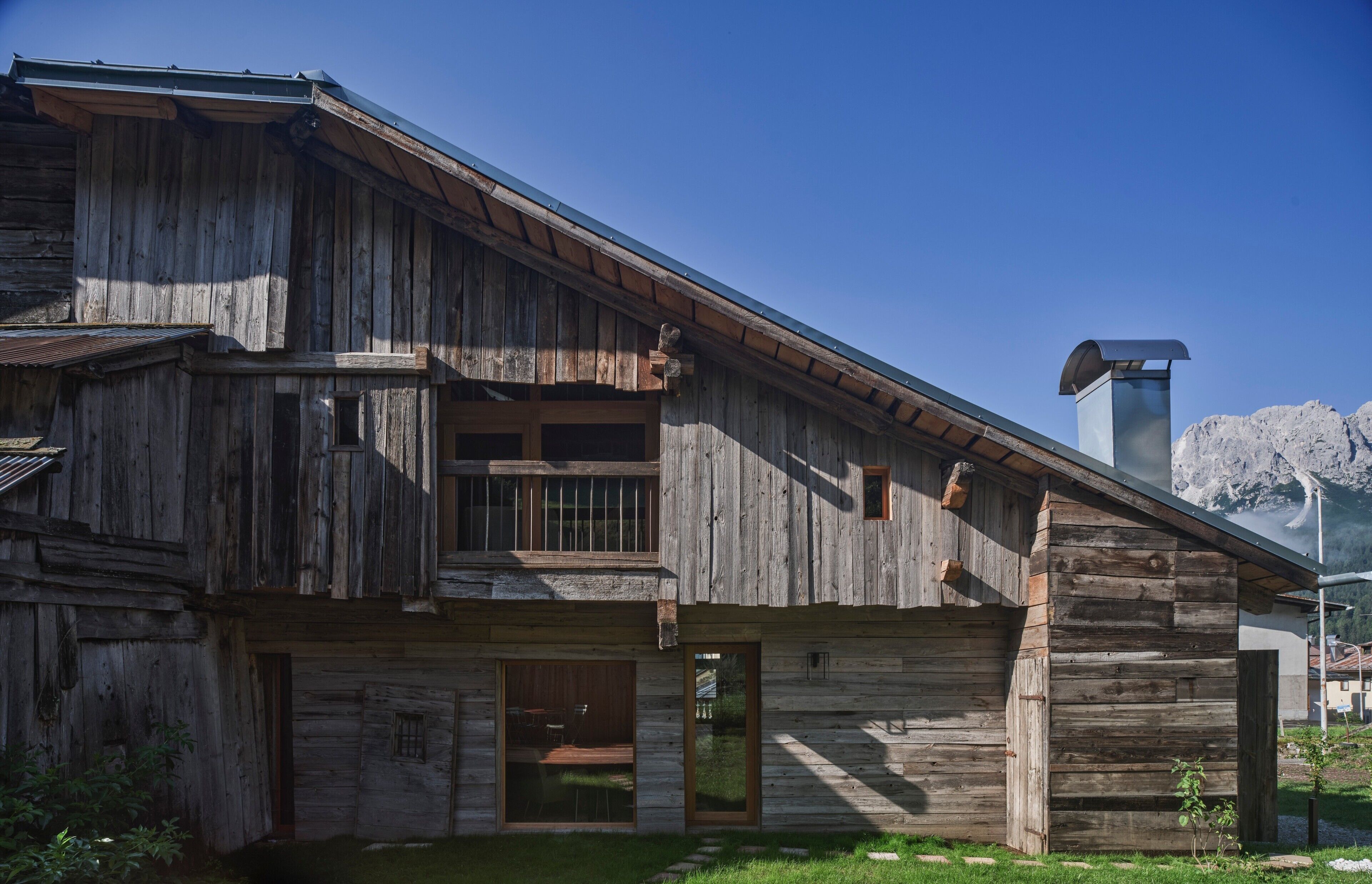 A rustic wooden building with a balcony, large windows, and a chimney.