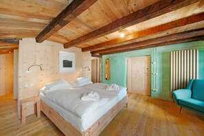 A wooden-paneled room with a large bed, a small table, and a teal chair.