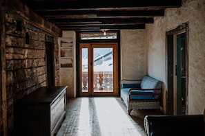 A rustic room with a wooden bench, a patterned sofa, and a view through a wooden door. - Room 'Fórnu' with Mountain View, Shared Terrace and Wi-Fi (Dosoledo)